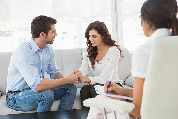 Engaged couple meeting counselor to discuss expectations, conflict patterns, and future planning, Couple reviewing relationship goals with counselor before marriage in a calm office